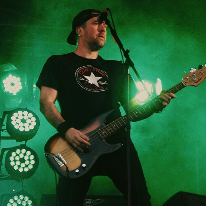 A man playing a guitar on stage at a music event with a green background and circle lights